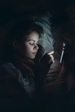 Девушка лежит в темноте с телефоном в руках