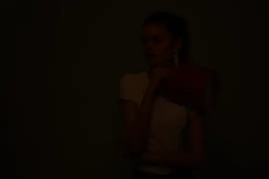 Молодая женщина в полумраке прижимает красную книгу к груди