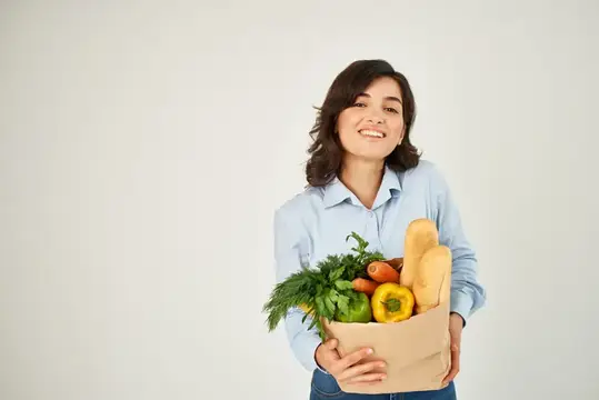 Улыбающаяся женщина с бумажным пакетом свежих овощей и хлеба