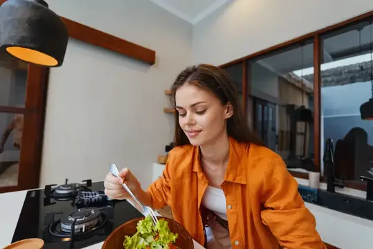 Молодая женщина в оранжевой рубашке ест салат на кухне