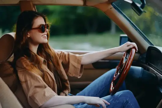 Улыбающаяся девушка в солнцезащитных очках за рулём автомобиля
