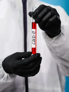 Лаборант в перчатках держит пробирку с анализом на COVID-19
