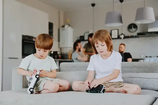 Два рыжеволосых мальчика играют с машинками на диване в гостиной