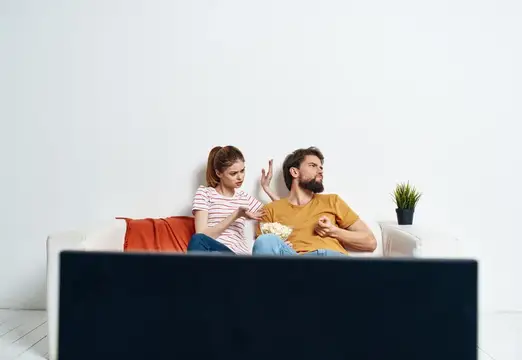 Мужчина и женщина ссорятся на диване перед телевизором