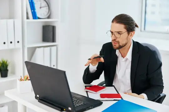 Мужчина в очках с длинными волосами работает за ноутбуком в офисе