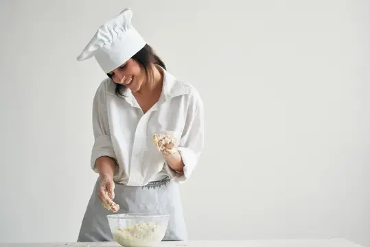 Улыбающаяся женщина в поварском колпаке лепит тесто на кухне