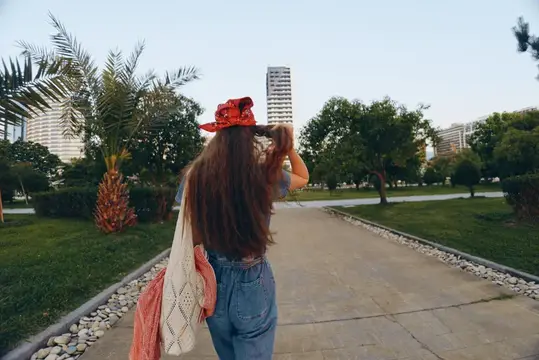 Женщина, одетая в современный богемно-вестерн джинсовый уличный стиль, идёт по городской дорожке в окружении зелени и небоскрёбов, демонстрируя яркую плёночную цветовую эстетику