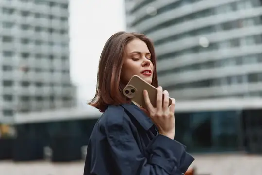 Молодая женщина с телефоном у лица на фоне высотных зданий
