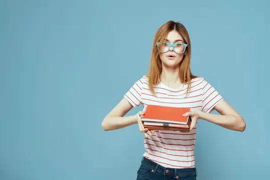 Рыжеволосая девушка в очках с книгами на голубом фоне