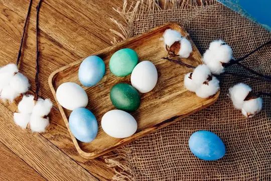 Пасхальные яйца на деревянном подносе среди веточек хлопка