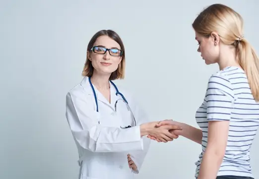 Женщина-врач и пациентка пожимают друг другу руки на светлом фоне, общаясь на тему медицины