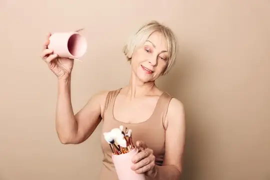 Седовласая женщина с кистями для макияжа на бежевом фоне