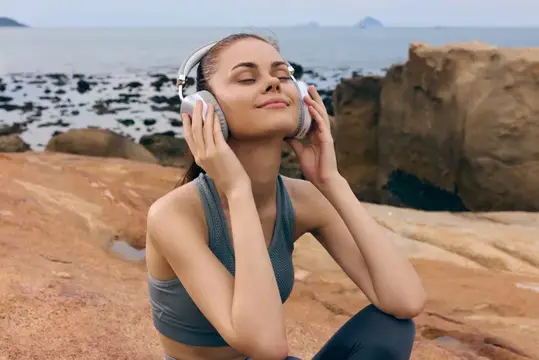 Блаженная молодая женщина в спортивной одежде слушает музыку в наушниках на скалистом берегу, излучая радость, что идеально подходит для концепций расслабления, природы и благополучия