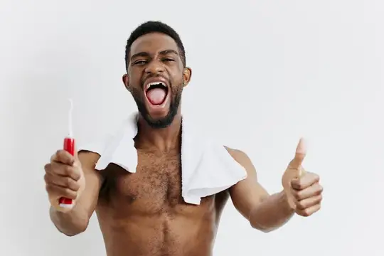 Улыбающийся темнокожий мужчина с зубной щеткой и полотенцем на плечах