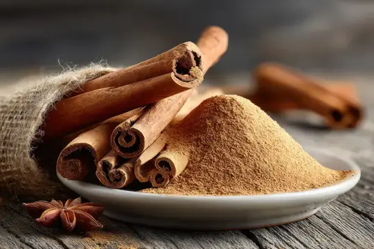 Палочки корицы и горка молотой корицы в белой тарелке на деревянном столе