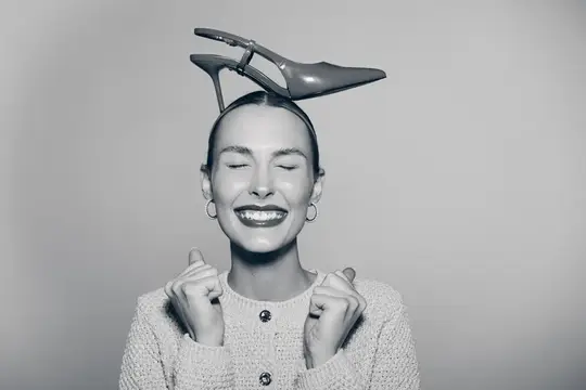 Улыбающаяся женщина с туфлей на голове держит кулачки