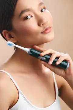 Азиатская девушка с электрической зубной щеткой у лица