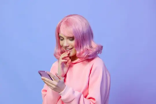 Девушка с розовыми волосами улыбается, глядя в телефон на сиреневом фоне