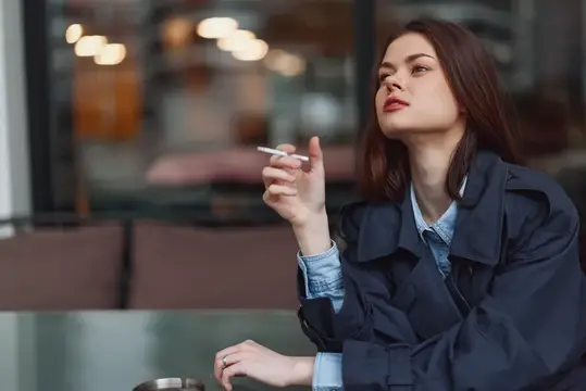 Молодая брюнетка с сигаретой в руке за столиком кафе