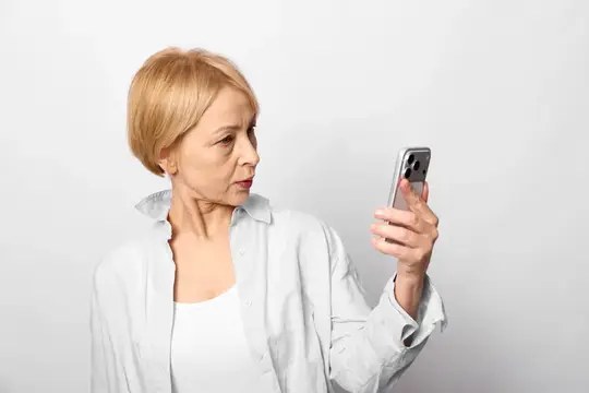 Блондинка в белой рубашке смотрит на смартфон с недоумением