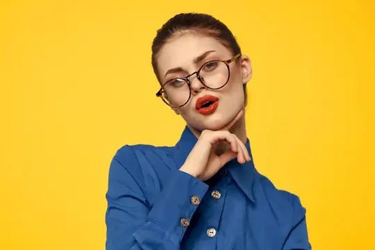 Молодая женщина в очках и синей рубашке на жёлтом фоне