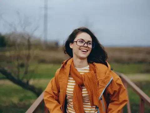 Смеющаяся девушка в очках и оранжевой куртке на улице