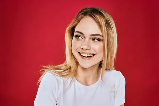 Улыбающаяся блондинка в белой футболке на красном фоне
