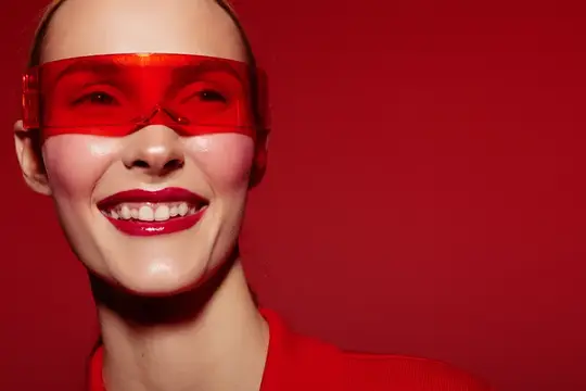 Улыбающаяся девушка в красных очках на красном фоне