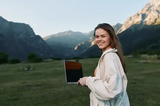Улыбающаяся девушка с ноутбуком на фоне гор
