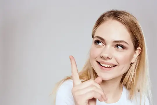 Светловолосая девушка улыбается и показывает пальцем вверх