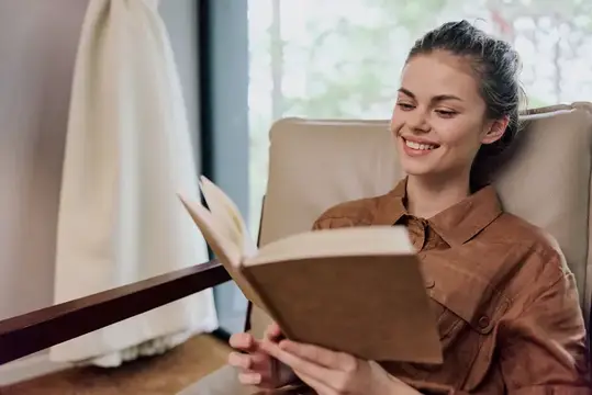 Улыбающаяся девушка с книгой в уютном кресле у окна