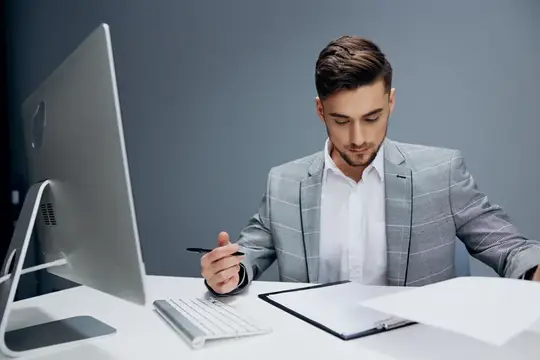 Молодой мужчина в сером пиджаке работает за компьютером в офисе