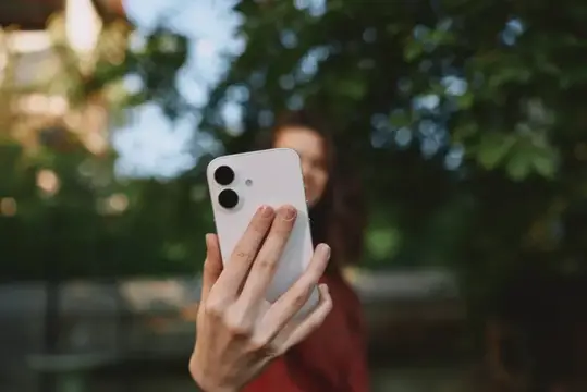 Девушка держит белый смартфон на фоне зелени