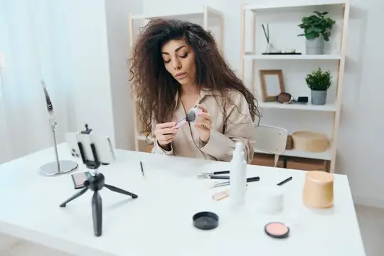 Кудрявая девушка записывает видео о макияже на смартфон
