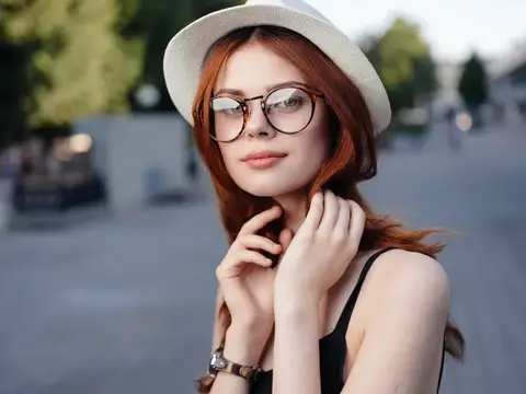 Рыжеволосая девушка в белой шляпе и круглых очках на улице