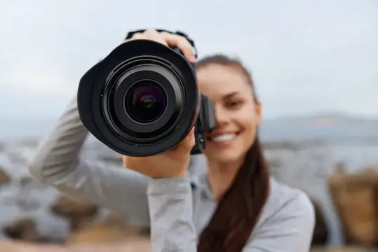 Улыбающаяся девушка смотрит в объектив фотокамеры на природе