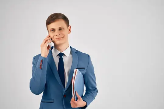 Молодой человек в синем костюме улыбается, разговаривая по телефону