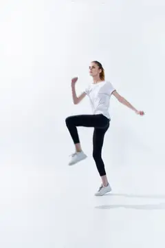 Молодая женщина в спортивной одежде выполняет упражнение с высоким подъемом колена