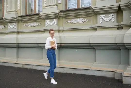 Симпатичная женщина в очках гуляет по городу с книгой, занимаясь образованием