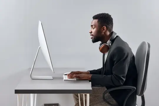 Темнокожий мужчина в наушниках работает за компьютером в офисе