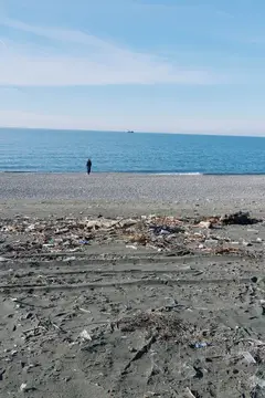 Одинокий человек стоит на галечном пляже среди мусора у моря