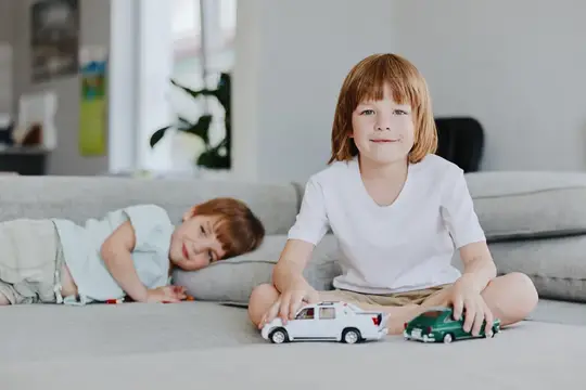 Рыжеволосый мальчик с игрушечными машинками на диване