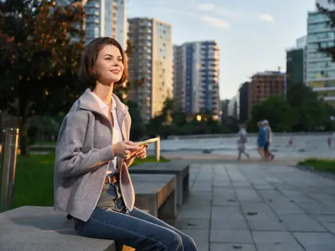 Уверенный молодой профессионал на открытом воздухе в залитой солнцем городской площади, печатающий на телефоне, спокойный и сосредоточенный, воплощающий современную рабочую жизнь и личный баланс…