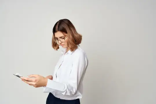 Молодая женщина в очках и белой рубашке смотрит в смартфон