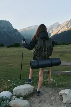Девушка с рюкзаком и треккинговой палкой смотрит на горы