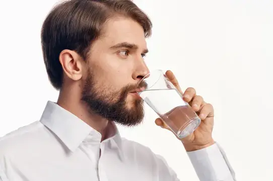 Бородатый мужчина в белой рубашке пьёт воду из стакана