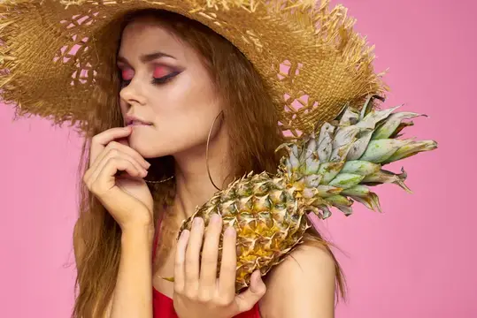 Девушка в соломенной шляпе с ананасом на розовом фоне