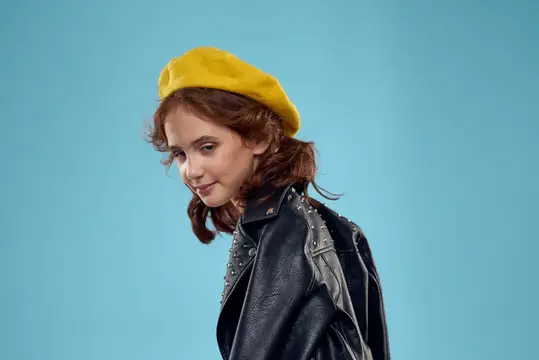 Рыжеволосая девочка в жёлтом берете и кожаной куртке на голубом фоне
