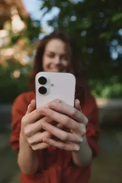 Улыбающаяся девушка держит белый смартфон на фоне зелени