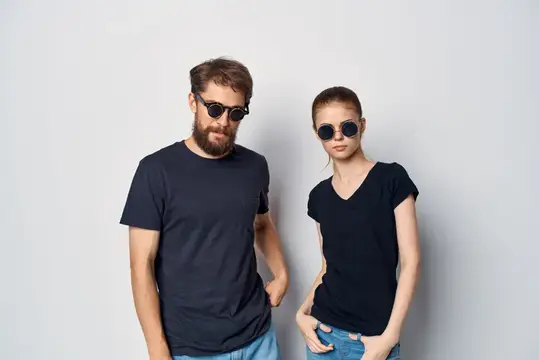 Модный мужчина и женщина в черных футболках и солнцезащитных очках позируют в студии, демонстрируя стиль жизни